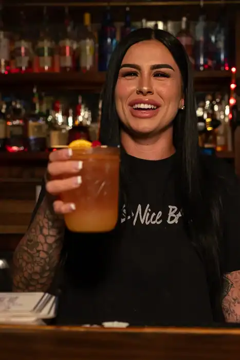 Bartender with long dark hair handing a drink to a customer at Q Bar