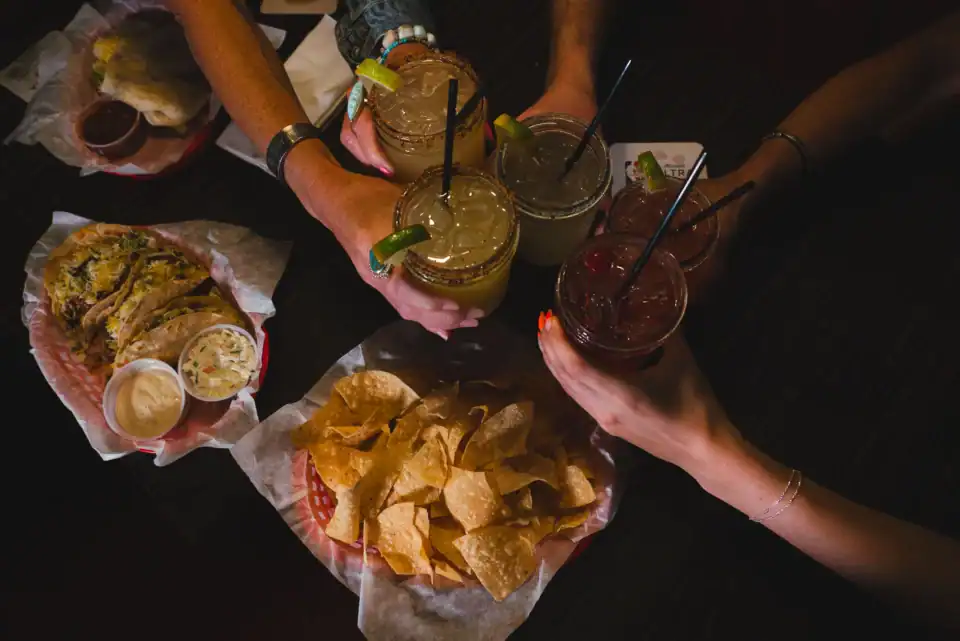 Tacos, chips, and friends going in for a cheers with cocktails at their table